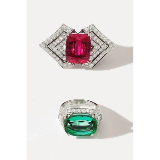 High-jewelry still-life shot: A diamond brooch with a ruby center and a diamond ring with a green tourmaline stone on a white surface.