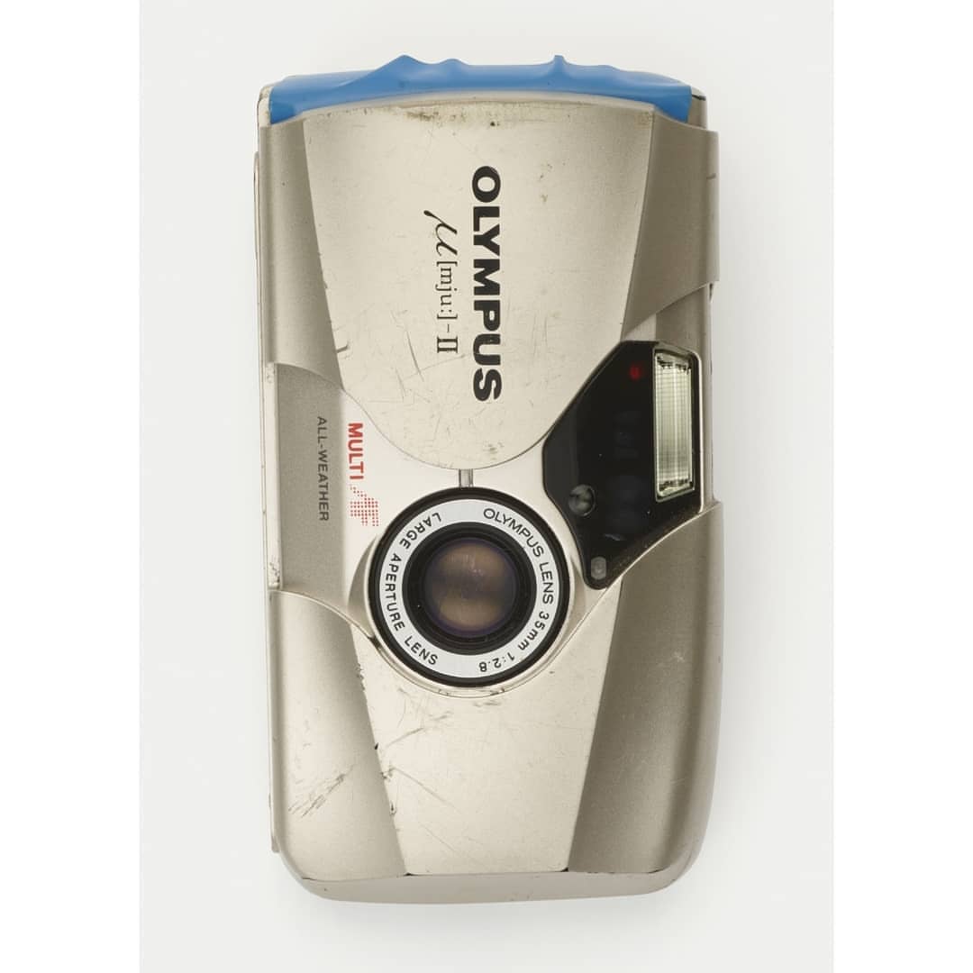 Silver Olympus [mju:]-II camera with a 35mm lens. Features include multi all-weather, large aperture. The camera sits on a white backdrop.