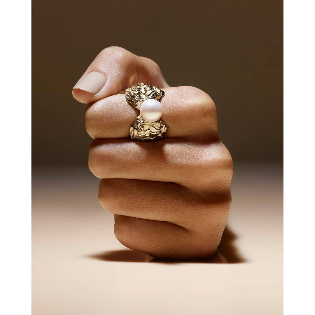 Close-up shot of a hand wearing a gold ring with a pearl, neutral background, jewellery shot, product photography for Visie platform.