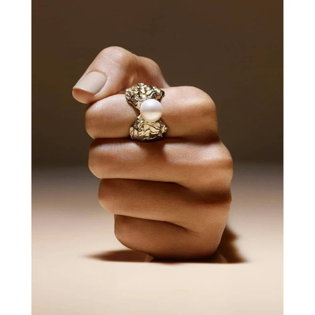 Close-up shot of a hand wearing a gold ring with a pearl, neutral background, jewellery shot, product photography for Visie platform.