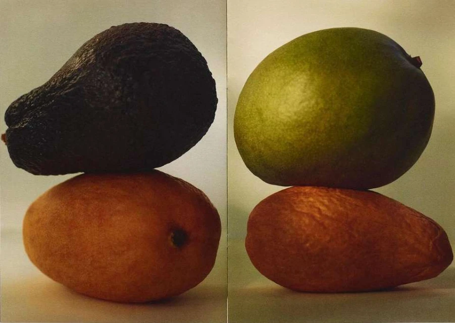 Two fruits stacked: a dark avocado atop a mango on the left, and a green mango atop another mango on the right, against a neutral background.