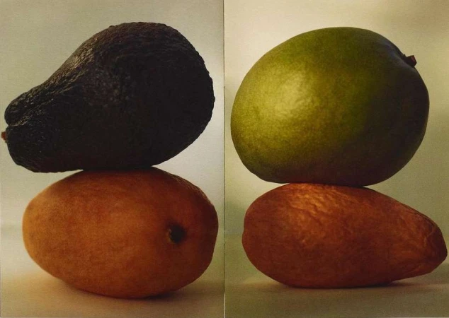 Two fruits stacked: a dark avocado atop a mango on the left, and a green mango atop another mango on the right, against a neutral background.