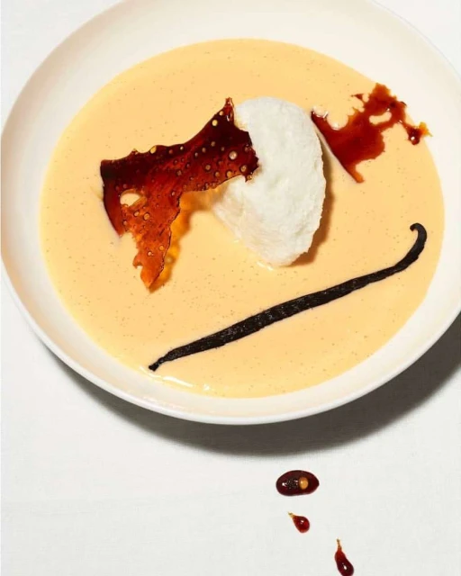Overhead shot of dessert featuring a white cloud-like meringue, caramelized sugar art, and vanilla bean in yellow cream sauce.