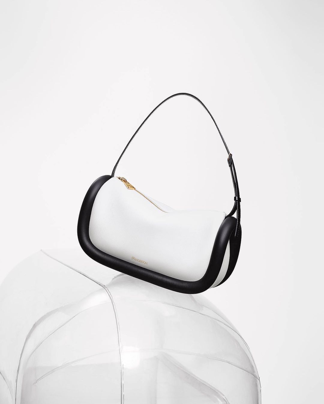 Fashion shot of a white handbag with black trim and black handle, resting on a clear, transparent sphere in a white photo studio.