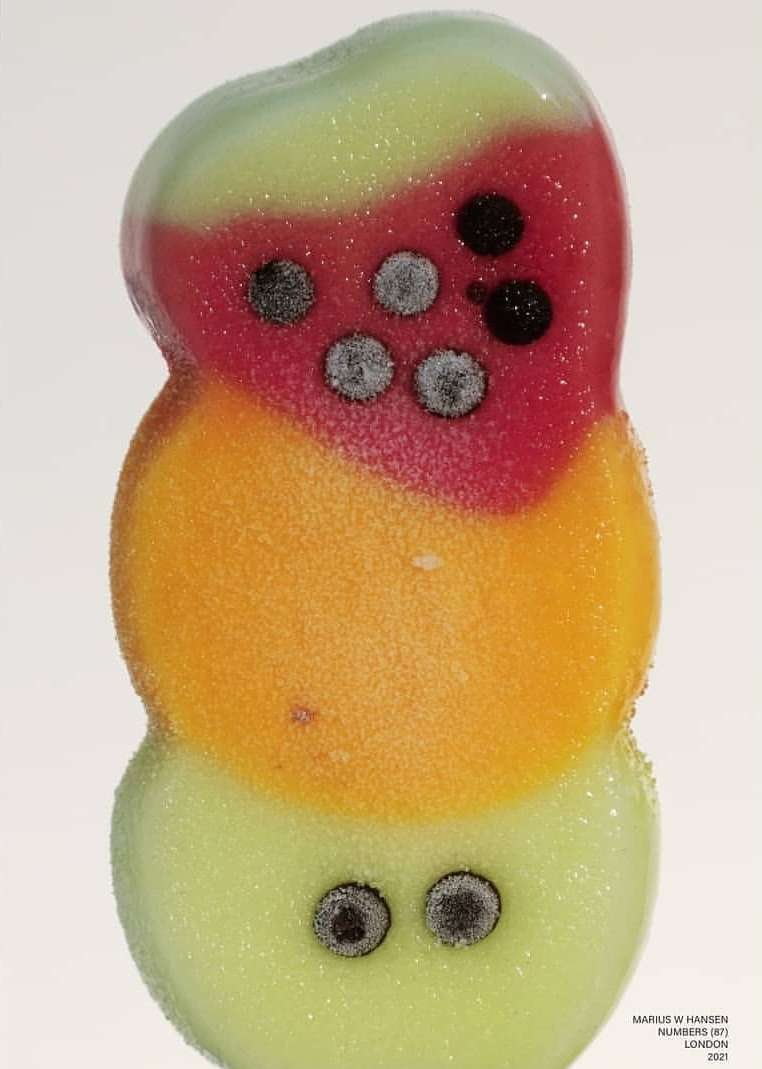 Close-up of colorful popsicle in the shape of a snowman, featuring red, orange, and light green sections with black dots.