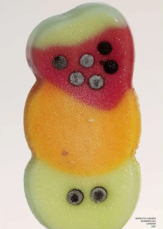Close-up of colorful popsicle in the shape of a snowman, featuring red, orange, and light green sections with black dots.