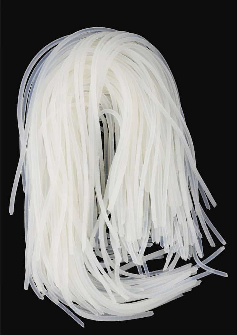 A pile of translucent, glutinous rice noodles on a black surface, showing the texture and shape of the noodles in detail.
