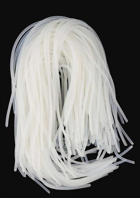 A pile of translucent, glutinous rice noodles on a black surface, showing the texture and shape of the noodles in detail.