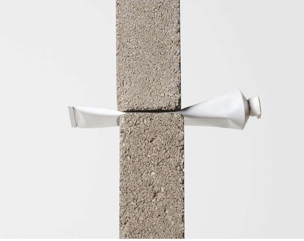 Minimalist studio shot of a white tube being squeezed between two concrete blocks on a white background, product photography, commercial.