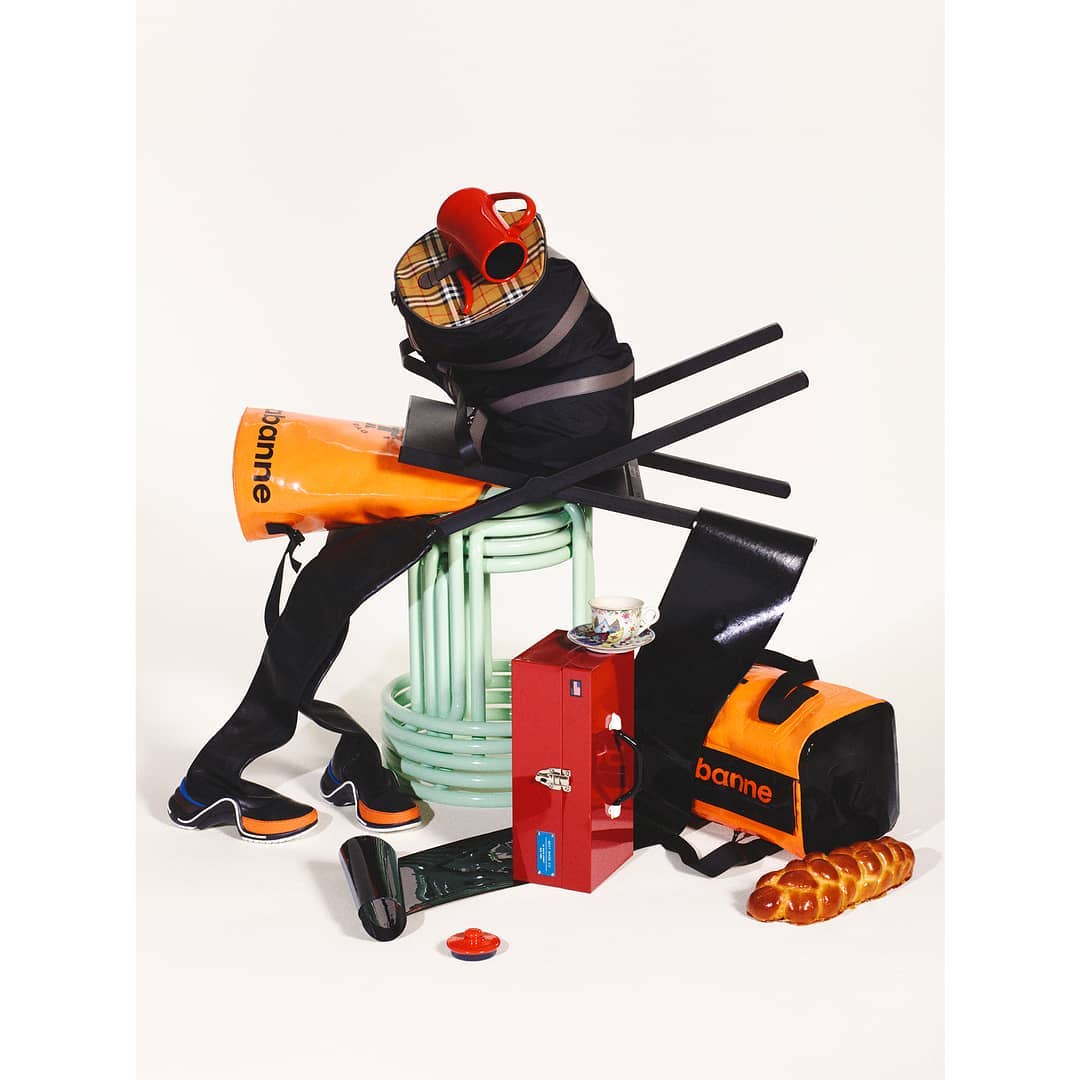 Still life featuring an arrangement of bags, shoes, and household objects against a white backdrop, creating a whimsical and surreal composition.