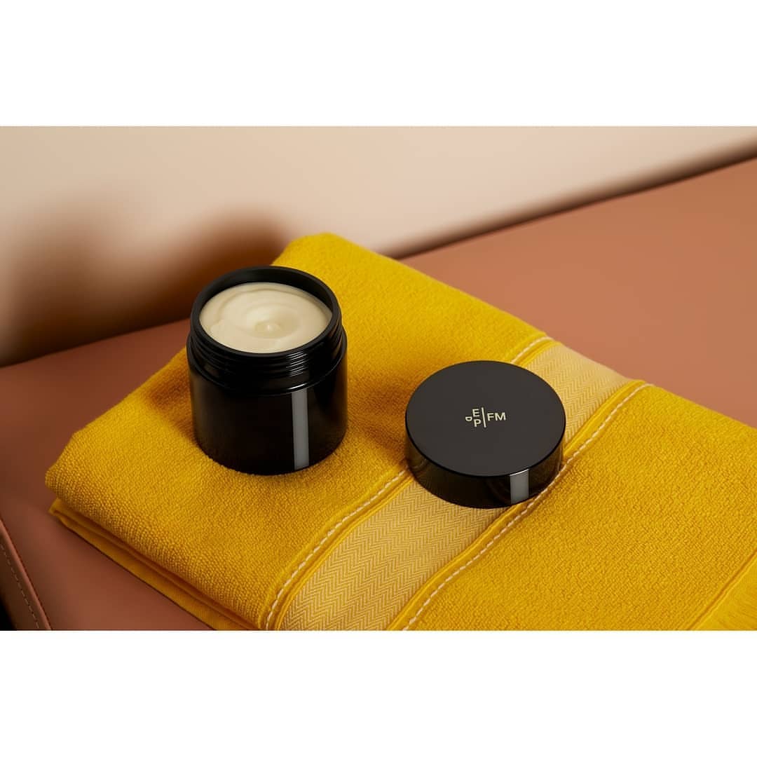 Cosmetic cream in a black container with a lid sits on a yellow striped towel against a two-tone background, product shot for beauty.