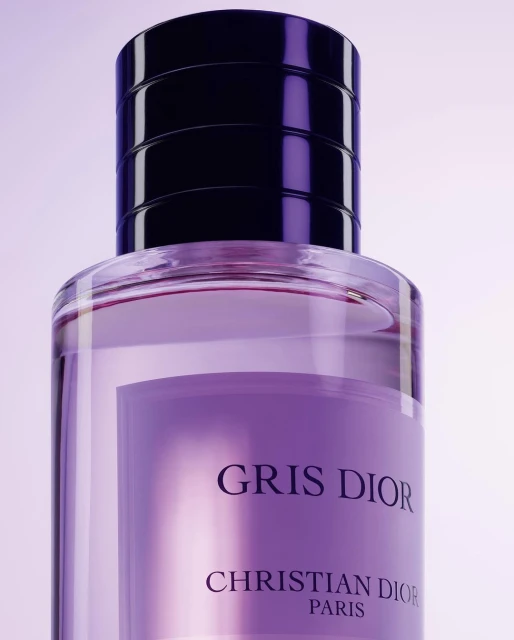 Close-up of a clear glass perfume bottle filled with light purple liquid, featuring a black cap and the logo Gris Dior Paris.