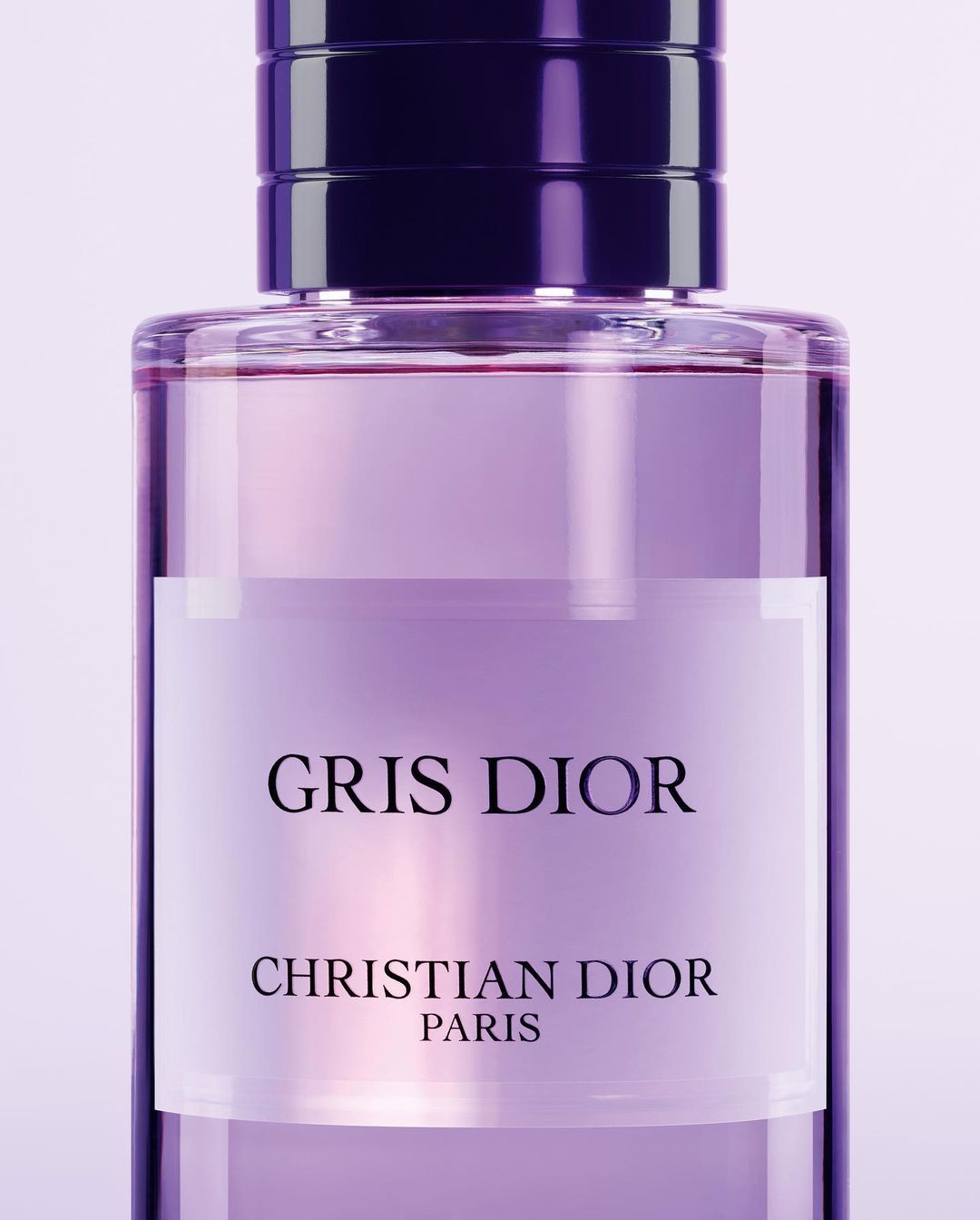 Close-up of a clear glass Dior perfume bottle filled with a pale purple liquid. The bottle features a dark purple lid.