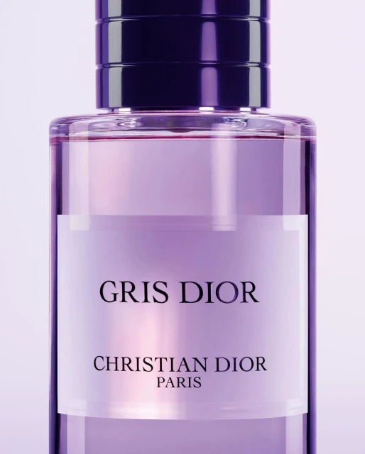 Close-up of a clear glass Dior perfume bottle filled with a pale purple liquid. The bottle features a dark purple lid.