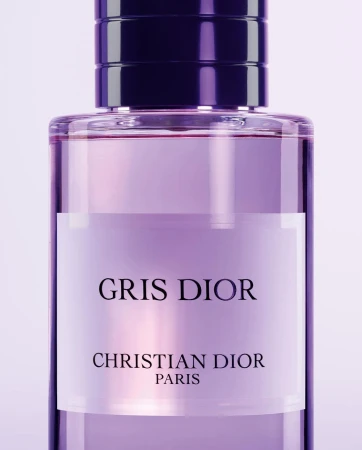 Close-up of a clear glass Dior perfume bottle filled with a pale purple liquid. The bottle features a dark purple lid.