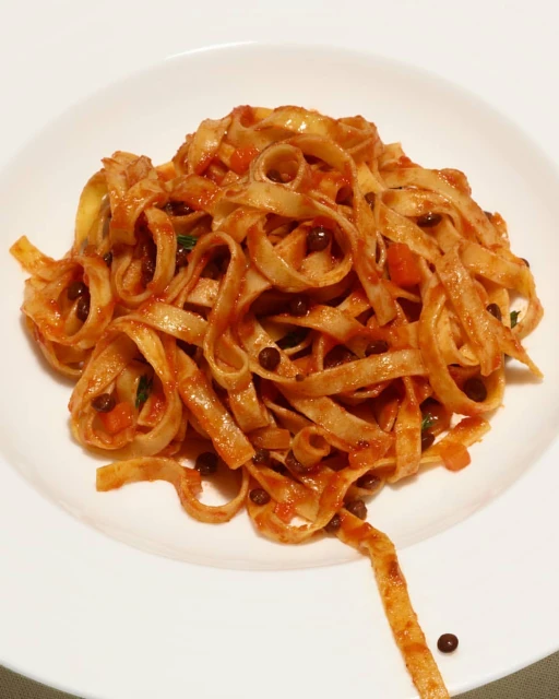 Overhead shot of tagliatelle pasta with tomato sauce and black lentils on a white plate. Italian cuisine concept, food photography.