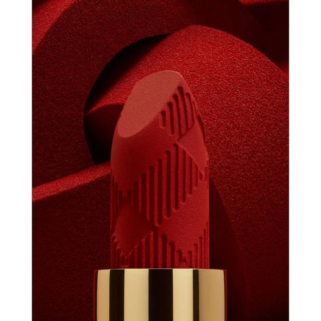 Macro shot of red lipstick with a patterned texture against a blurred red background, showcasing beauty and cosmetic product details.