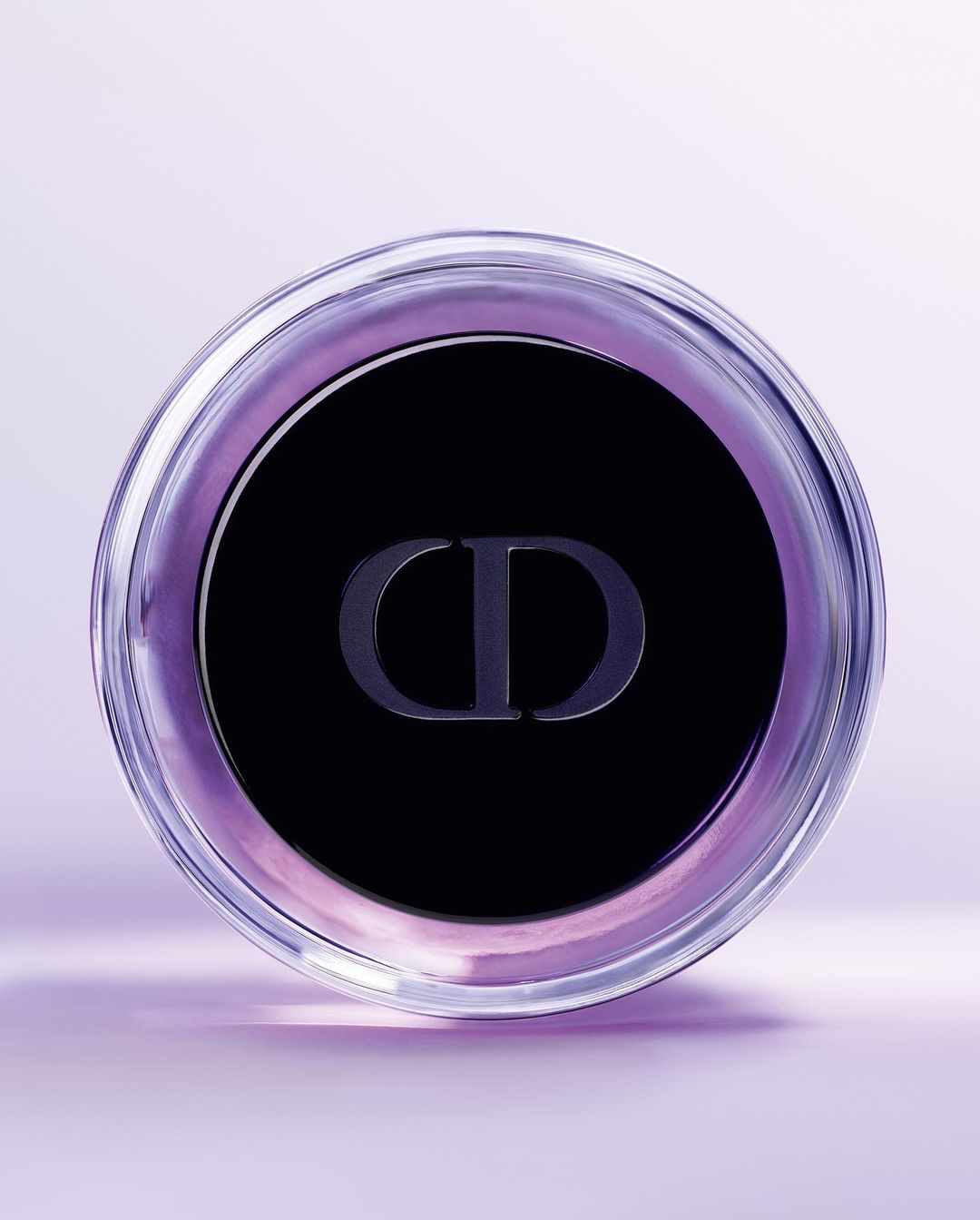 Close-up of a clear glass container with a black lid and the 'CD' logo, set against a soft lavender background, emphasizing beauty and luxury.