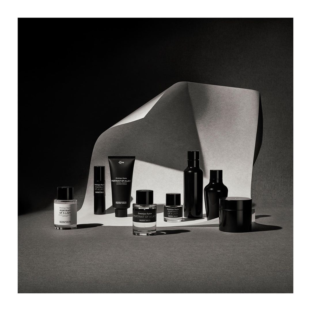 Monochromatic product shot featuring an array of perfume and skincare bottles against a textured paper backdrop with shadow play.