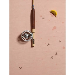 Fly fishing rod with silver reel laid vertically on a pink fabric background with scattered metal hooks and a lemon wedge.