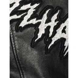 Macro view of black leather jacket with white textured applique lettering and visible seam by Marius W Hansen