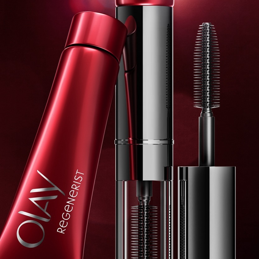Close-up of OLAY Regenerist product showing a red tube and a black and silver mascara wand with spiral brush for beauty advertising.