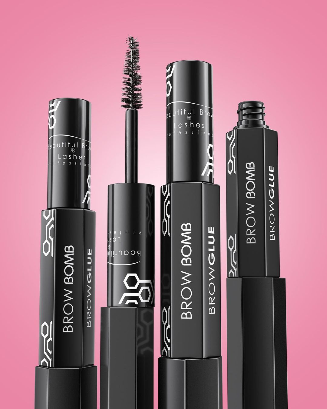Multiple black tubes of Brow Bomb Browglue mascara with an open applicator on a pink background in a beauty product shot.
