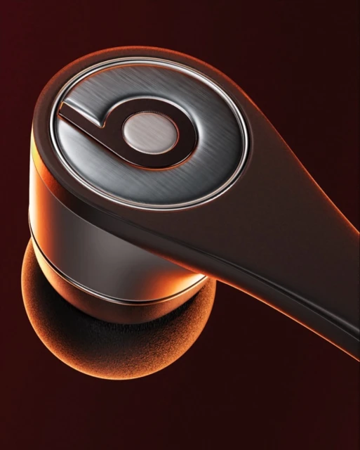 Close-up of a black and gray Beats Studio Buds earbud showing the metallic finish, product logo, and in-ear fit on a gradient red background.