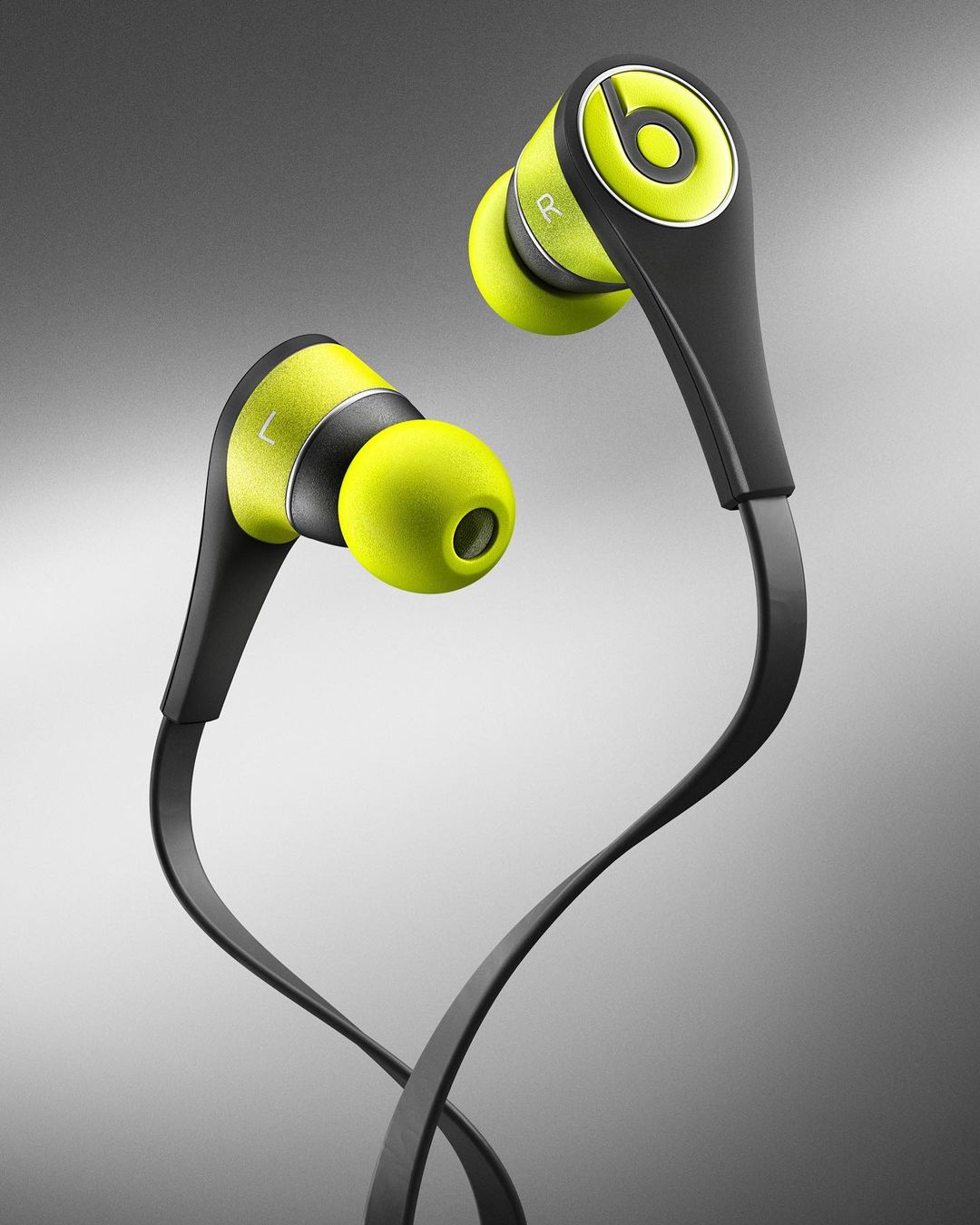 Studio shot of black and neon yellow Beats in-ear headphones with the 'b' logo, against a gradient gray background.