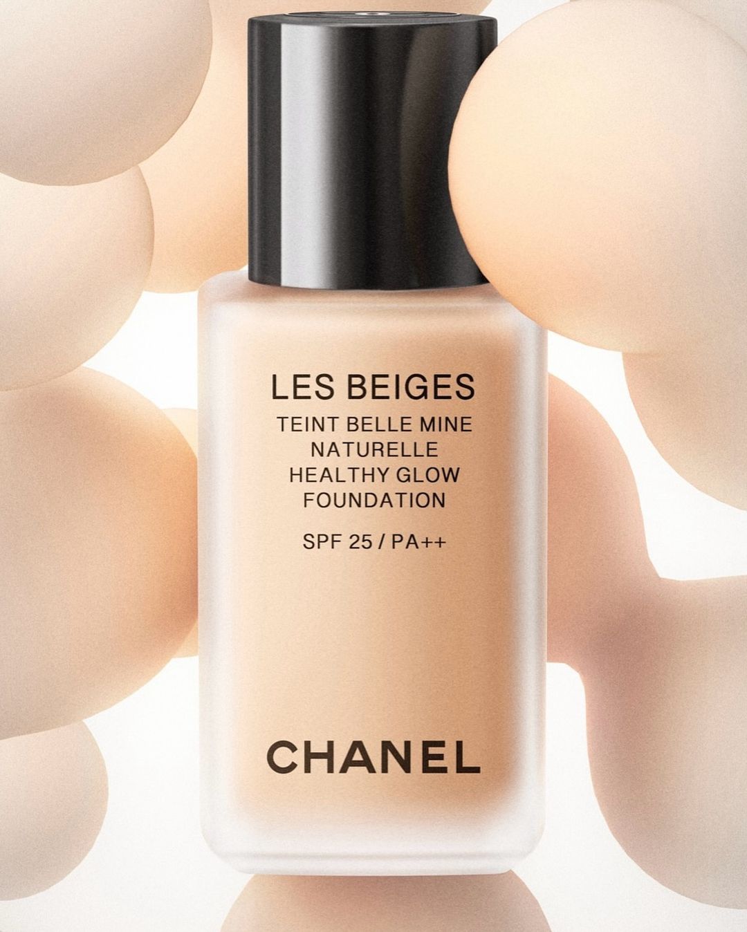 Chanel Les Beiges Teint Belle Mine Naturelle Healthy Glow Foundation bottle in a studio shot, surrounded by peach-toned spheres.