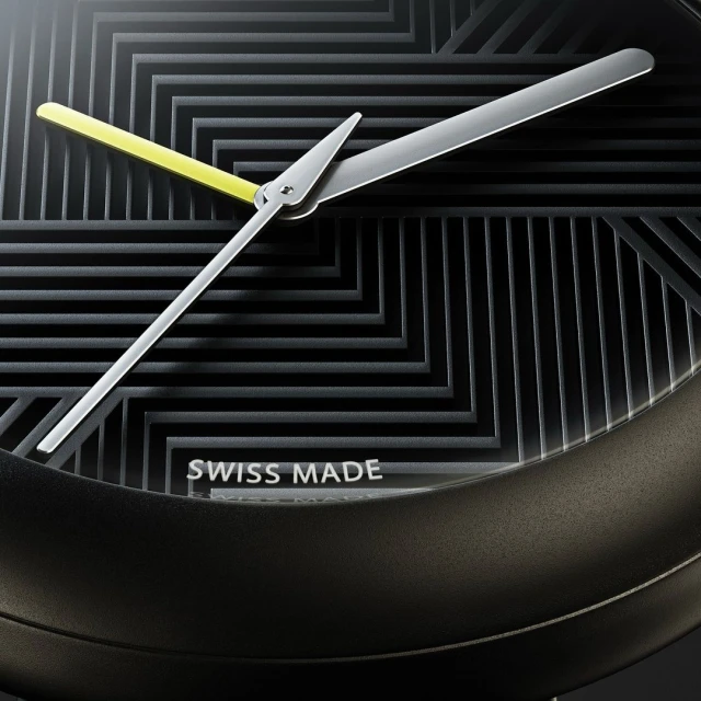 Close-up of a black and gray watch face with yellow second hand and silver minute and hour hands against a geometric dial.