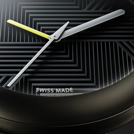 Close-up of a black and gray watch face with yellow second hand and silver minute and hour hands against a geometric dial.