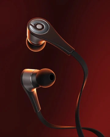 Close-up studio shot of black Beats in-ear headphones with silver accents against a blurred gradient red-orange background. Product photography.