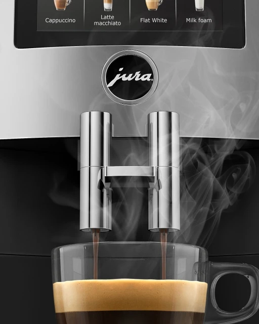 Espresso pours into a glass cup from a Jura coffee machine, close-up, with visible steam and coffee options displayed on the machine.