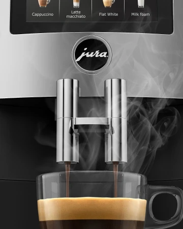 Espresso pours into a glass cup from a Jura coffee machine, close-up, with visible steam and coffee options displayed on the machine.