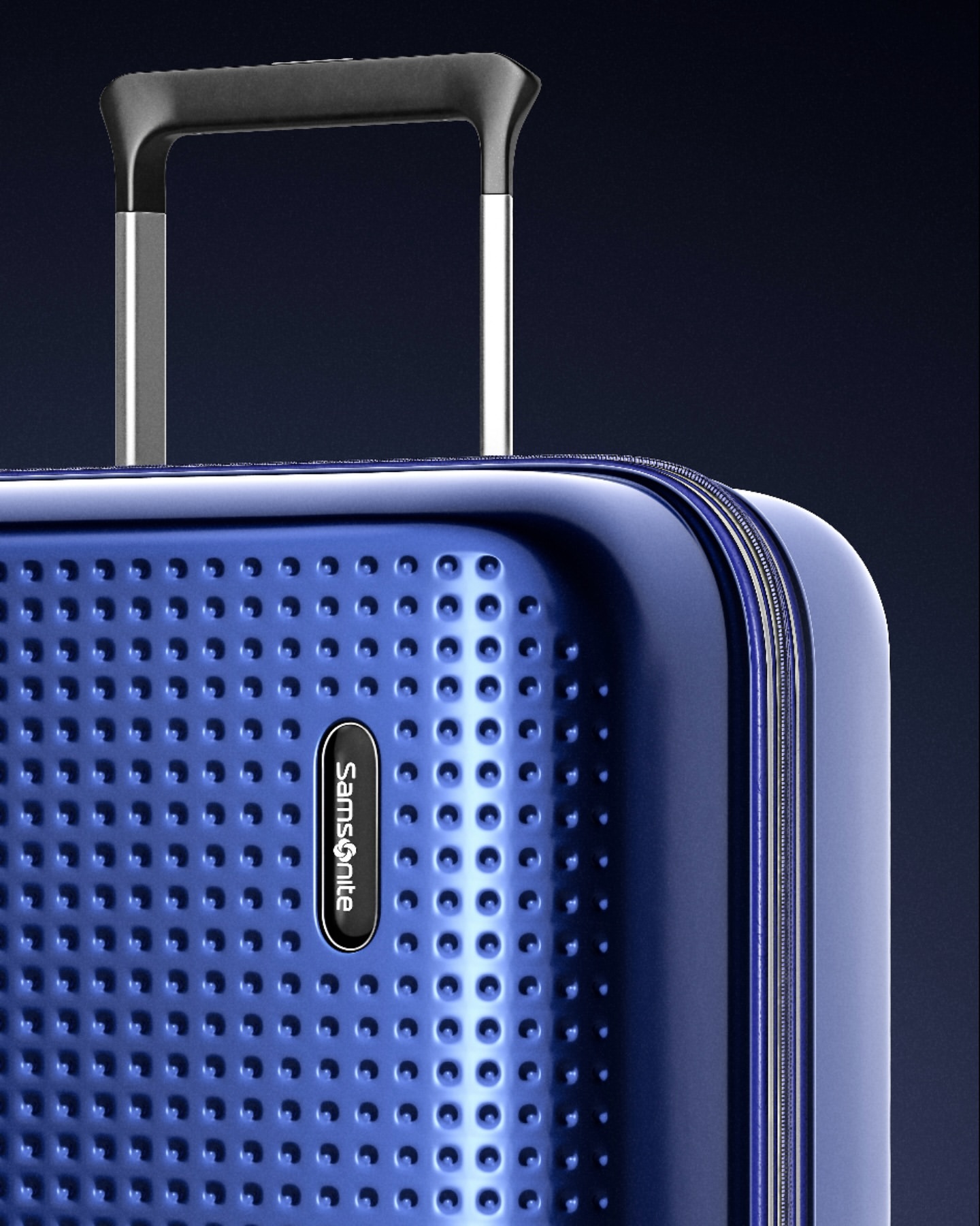 Close-up of a blue Samsonite suitcase showing the textured surface, logo, telescoping handle, and metallic frame details against a dark background.