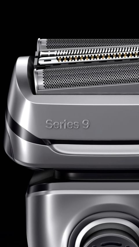 Close-up of a silver Braun Series 9 electric razor head featuring multiple cutting elements and a textured surface against a black backdrop.