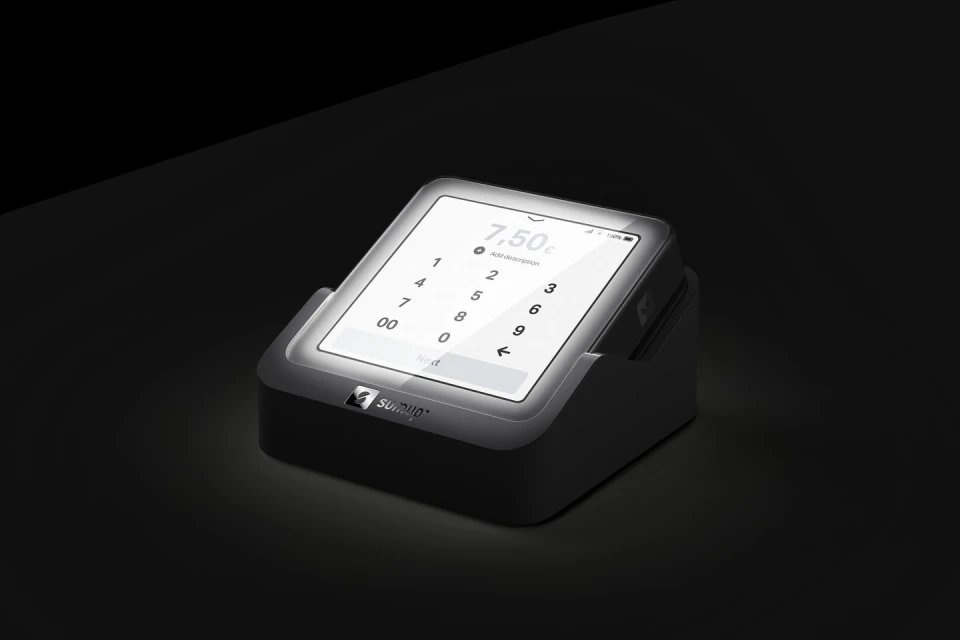 A digital payment terminal displays a keypad and a monetary value of 7.50 against a dark, shadowy background in a studio product shot.
