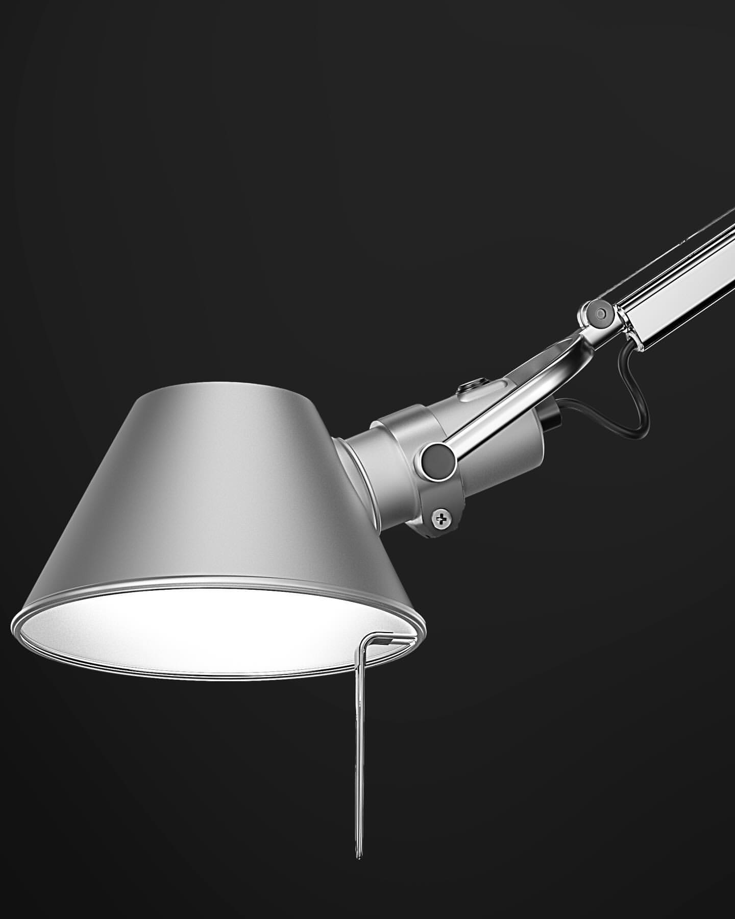 Silver adjustable table lamp against a dark background with white light emanating from underneath the lamp shade.