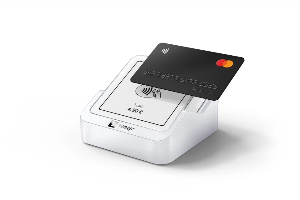 Close-up of a black credit card resting on a white SumUp card reader, isolated on a white background, displaying a contactless payment.