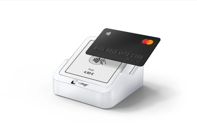 Close-up of a black credit card resting on a white SumUp card reader, isolated on a white background, displaying a contactless payment.