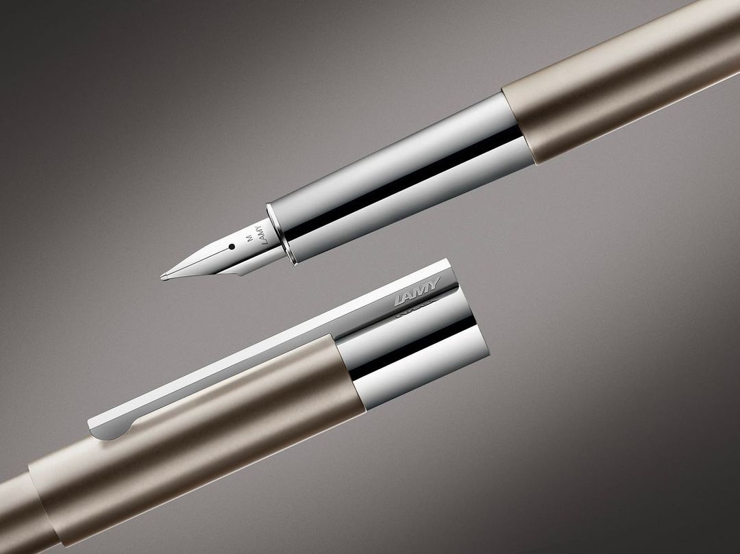 Close-up of a luxurious silver and gold LAMY fountain pen with its cap partially open, presented against a soft grey backdrop.