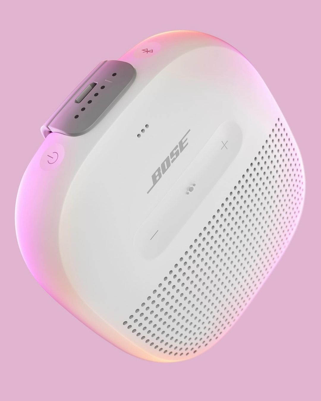 Close-up studio shot of a white Bose Bluetooth speaker against a pink background with colorful rim lighting effect emphasizing its features.