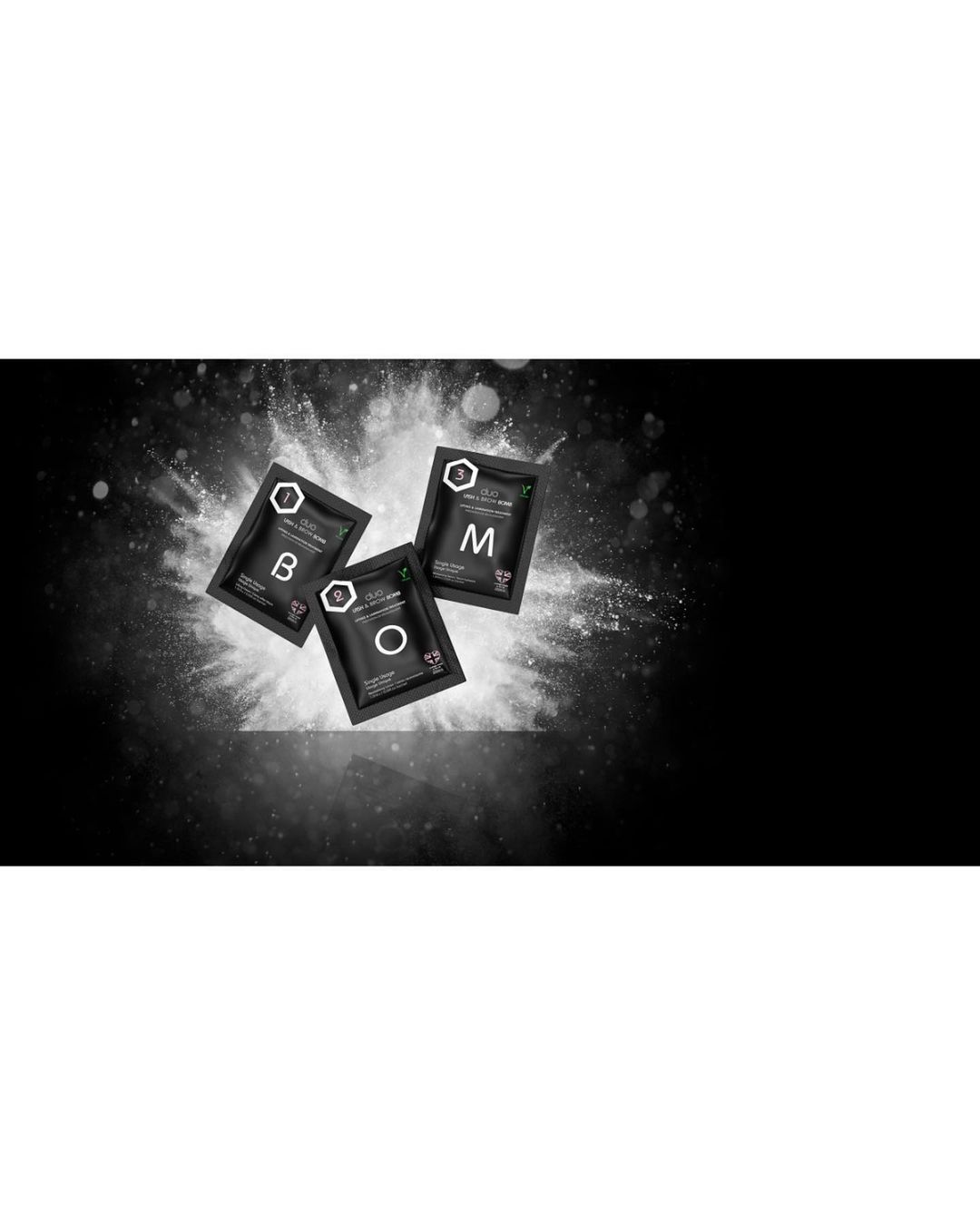 Close-up shot of three black cosmetic sachets featuring the letters B, O, and M, displayed against a textured dark background with a white powder effect.