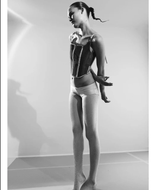 Monochrome portrait of a woman in a corset, posing against a clean studio backdrop, emphasizing high fashion and elegant styling in black and white.
