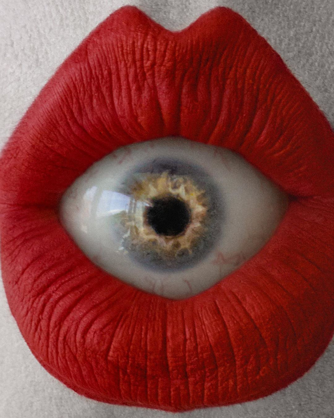 Surreal eye inside red lips art. Macro close-up of human eyeball replacing teeth, surrounded by lipstick. Creative makeup concept.