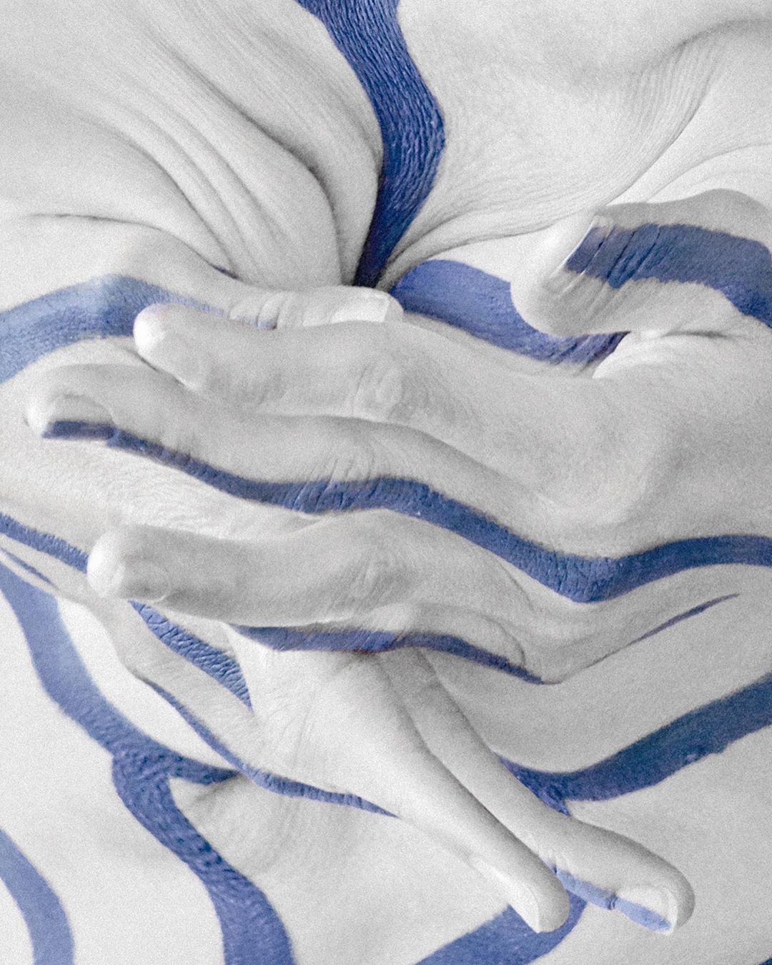 Close-up abstract image of a fair-skinned human torso and hands painted with white and blue wavy stripes in a studio setting.