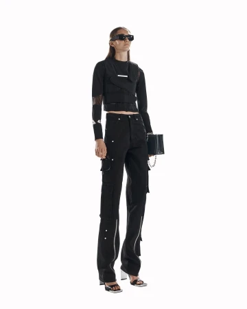 Fashionable woman poses in black top and cargo pants with silver details, holding a matching black purse against a white backdrop.
