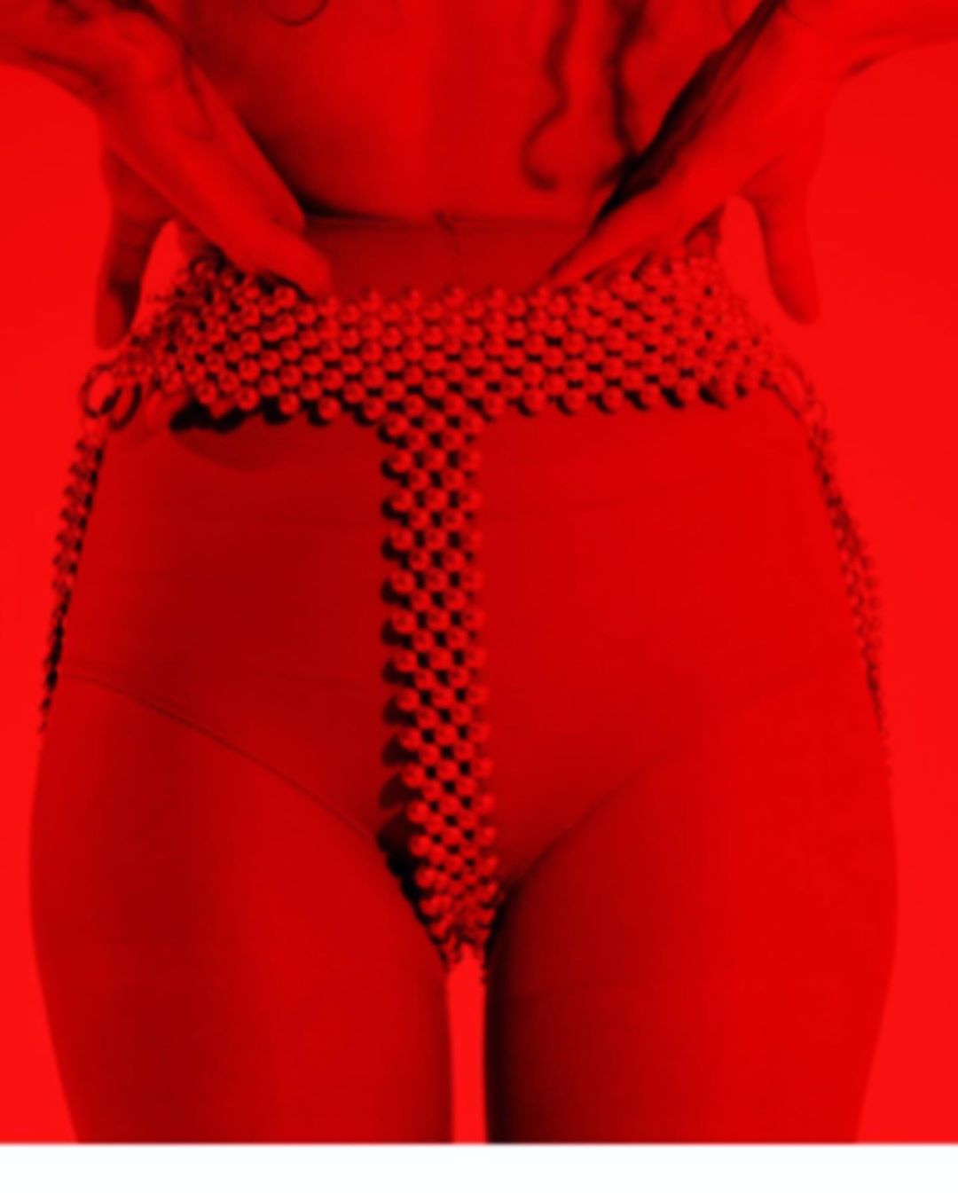 Close-up on the midsection of an adult, clad in a red swimsuit and a beaded belt, set against a monochromatic red background.