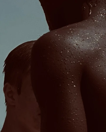 Close-up portrait of two individuals with water droplets on skin against a muted sky background by Mariya Pepelanova